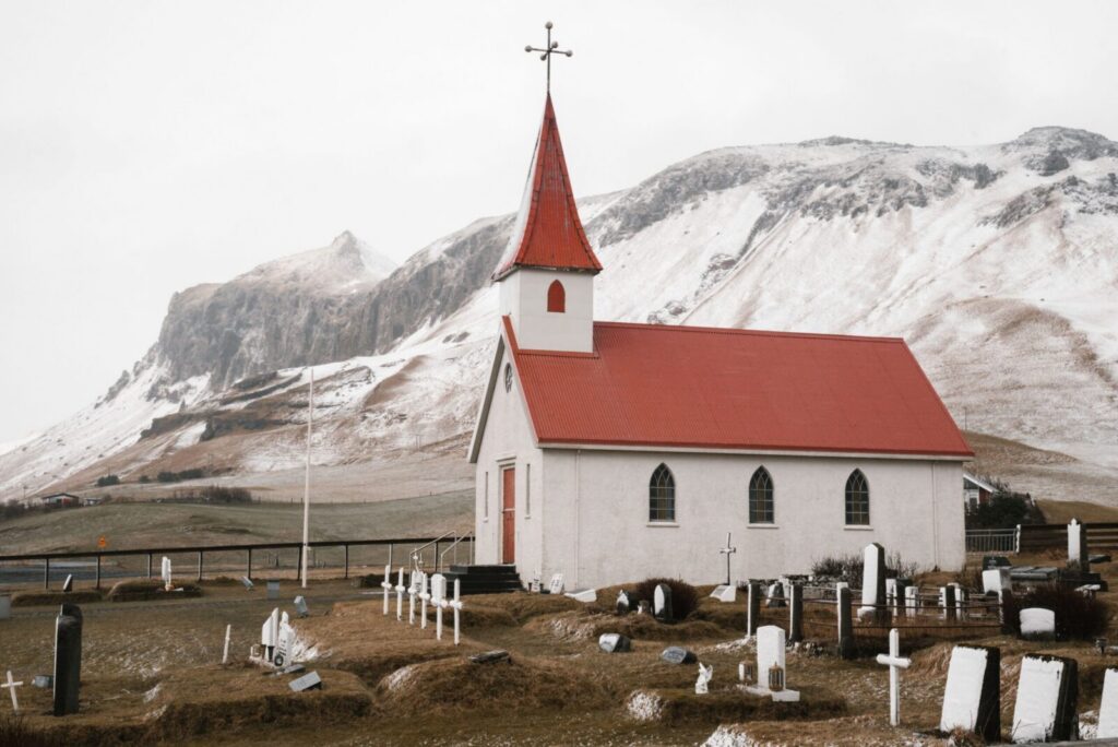 Dyrholaey Church and quiet churchyard with cemetery near magnificent snowy mountains on cloudy autumn day in Iceland